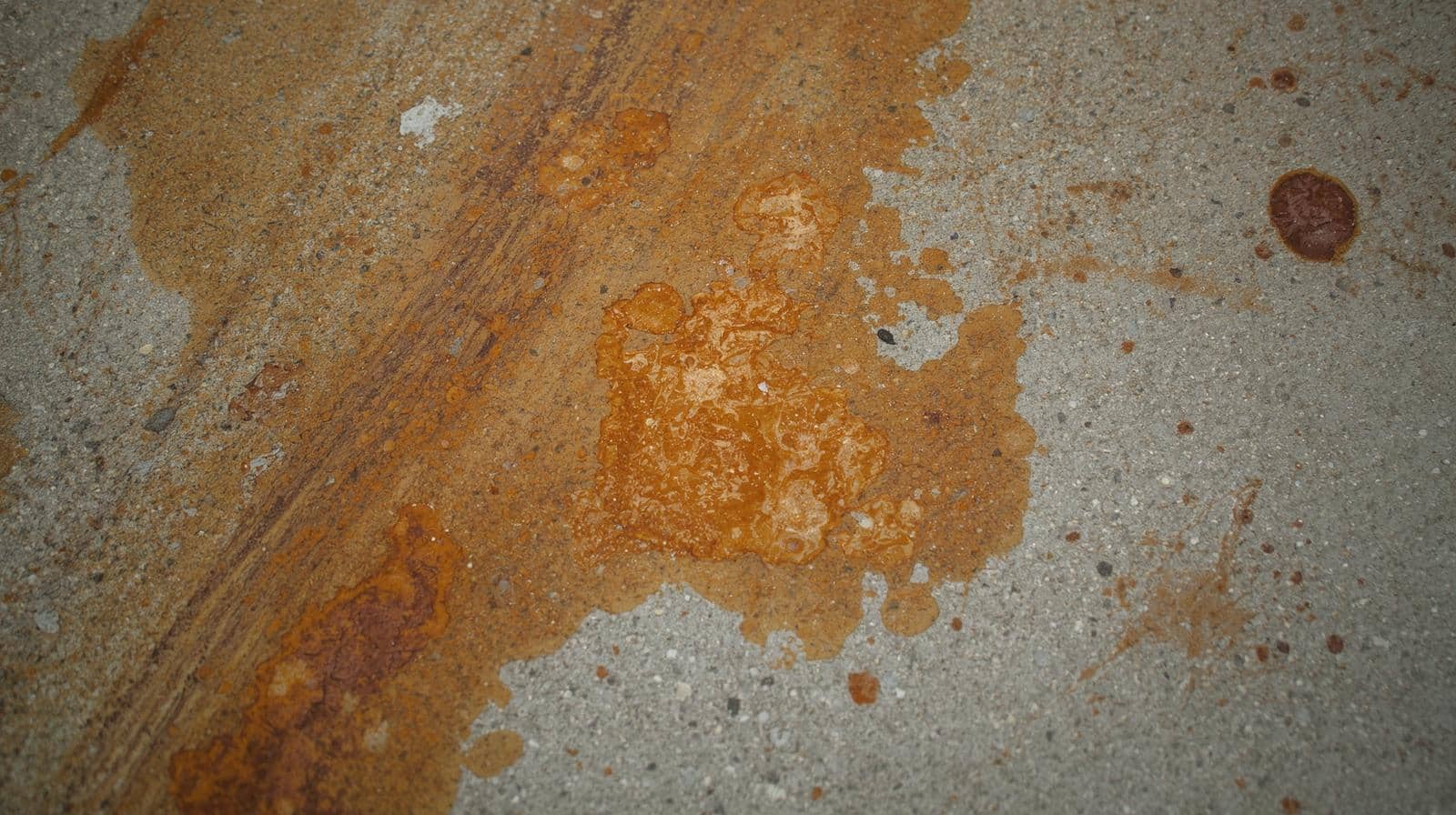 Orange bore water stains on concrete driveway before treatment with stain remover Description: Wide shot showing typical bore water staining on a concrete driveway with orange-brown discolouration